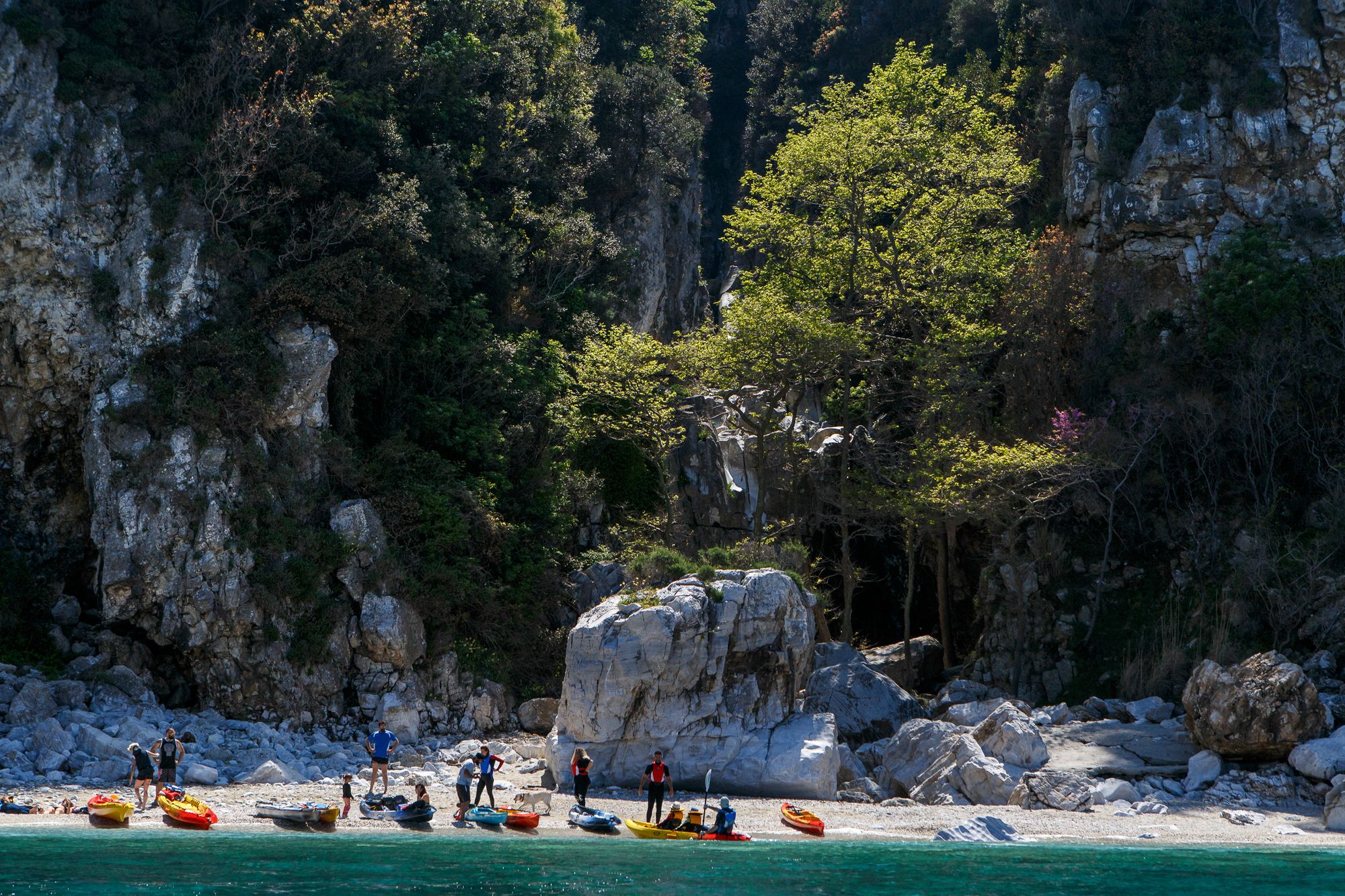 Un gruppo di kayakisti su una spiaggia con sfondo roccioso nella penisola di Pelion, in Grecia.