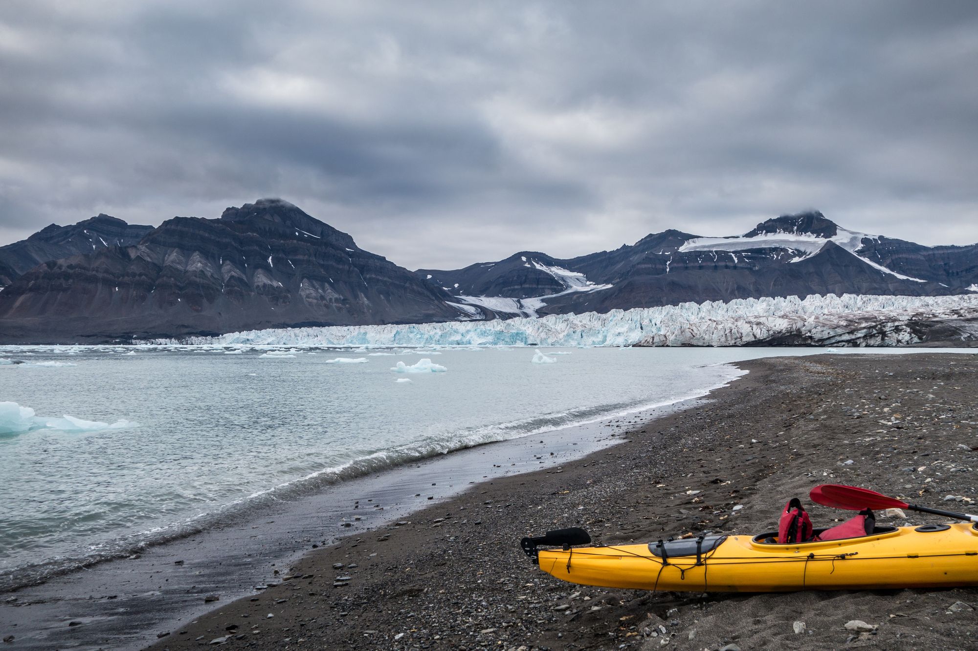 Un kayak su una spiaggia buia delle Svalbard, con ghiacciai e montagne sullo sfondo.