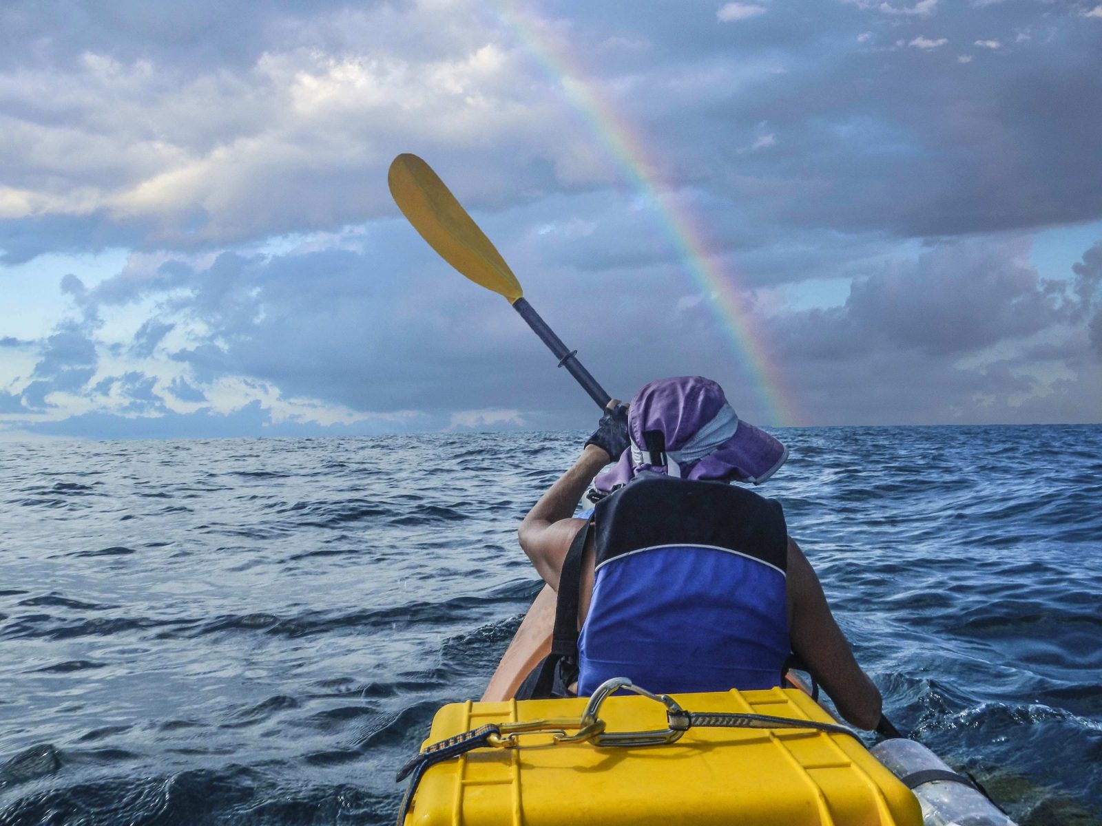 Un kayaker nell'oceano, con un arcobaleno davanti a sé. 