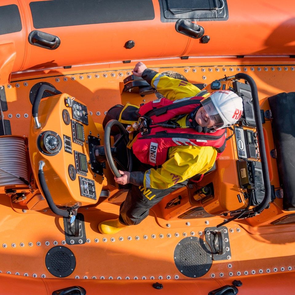 Donna al timone di una scialuppa di salvataggio della RNLI con indosso l'equipaggiamento di sicurezza.